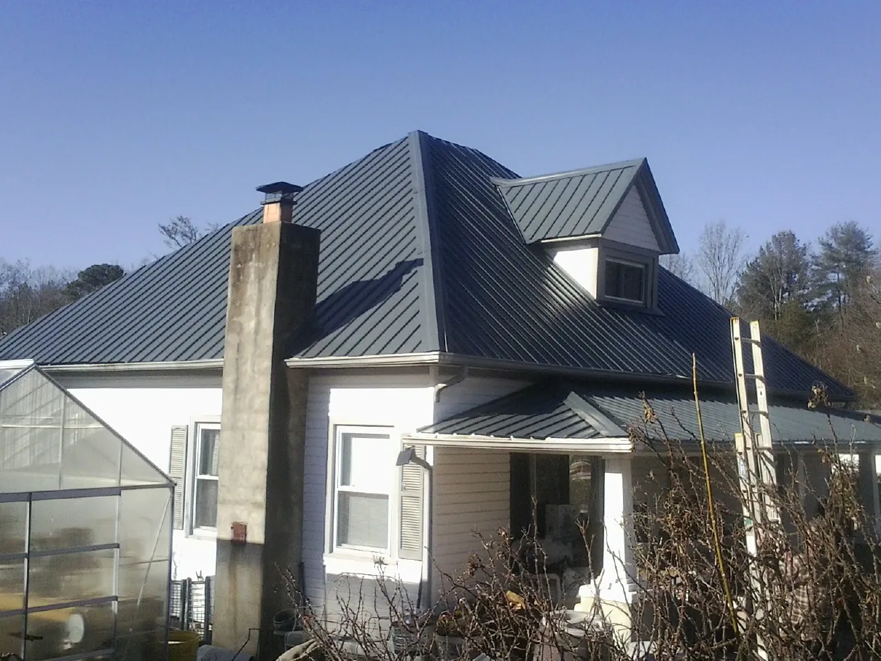 Dark blue standing seam metal roof on a white farmhouse with dormer in Ernul