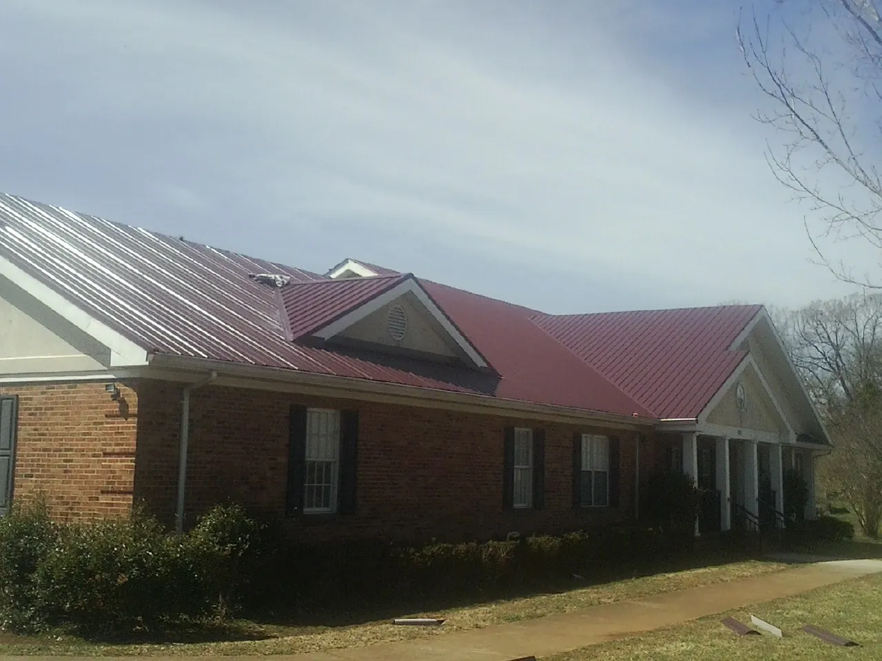 Red metal roof with gabled entries on a long brick building, from a Hail Damage Roof Repair job in Ernul
