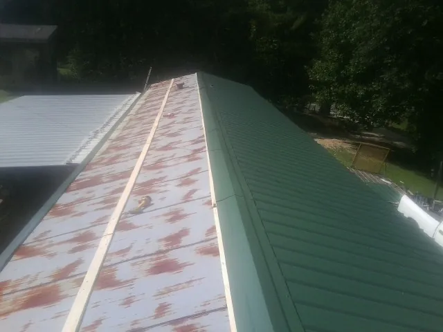 Old rusted panels beside newly installed green metal roofing — Wind Damage Roof Repair by Roofing Brothers in Ernul