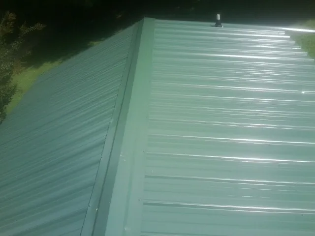 New green metal panels meeting at the ridge of a roof — Flat Roof Repair work by our crew in Ernul