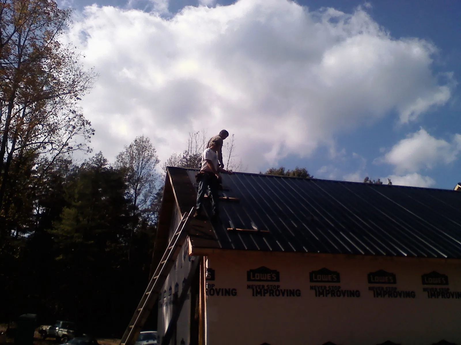 Roofer fastening dark metal panels high against a cloudy sky, from a Roof Inspection job in Ernul