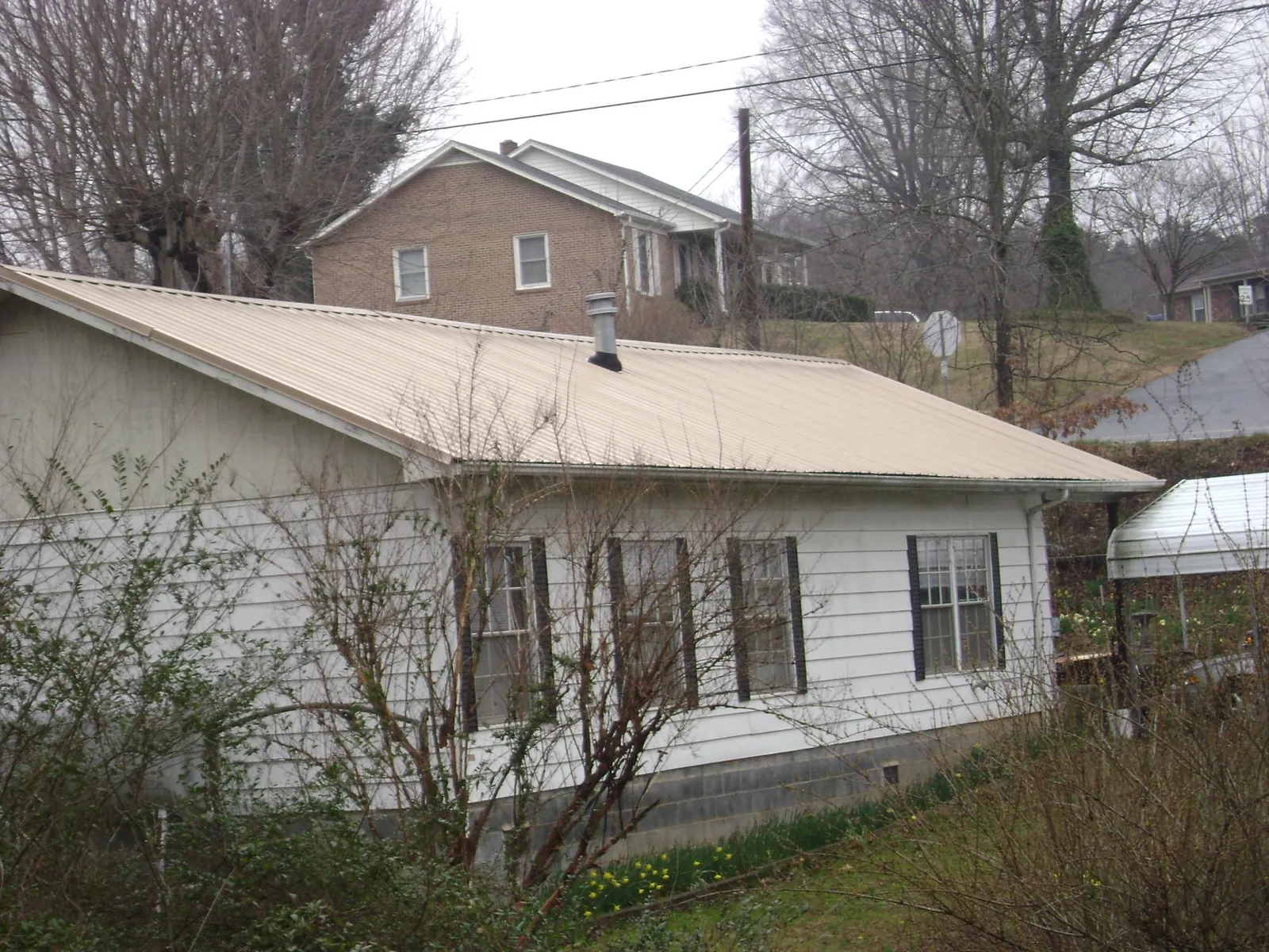 Tan metal roof on a white sided house set into a hillside — Commercial Roofing by Roofing Brothers in Ernul