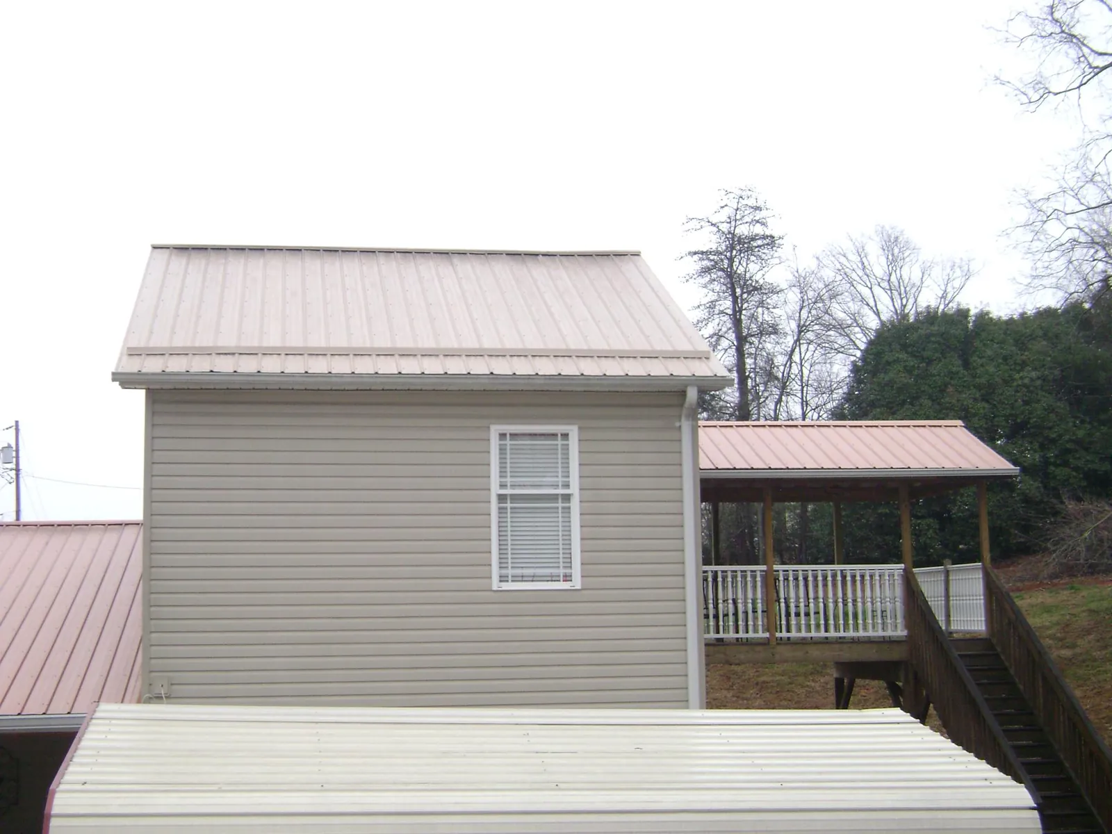 Tan metal roofs on a two story addition and attached porch, from a Roof Replacement job in Ernul